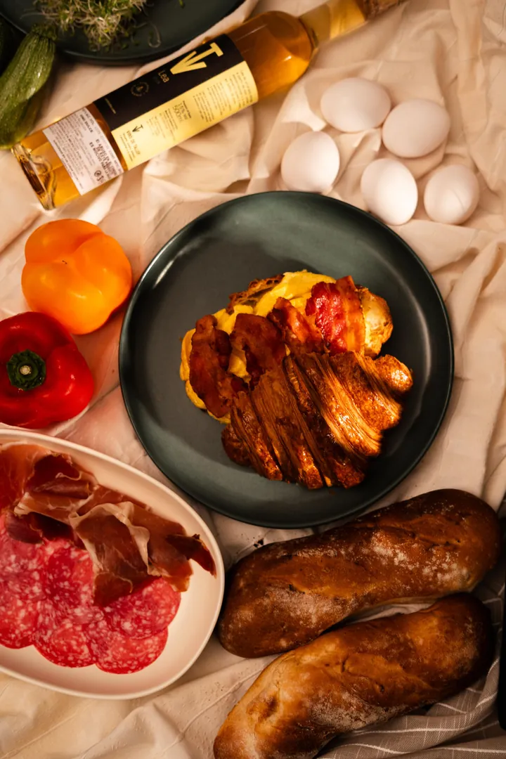 Croissant con huevo y tocino rodeado de pan, embutidos y pimientos